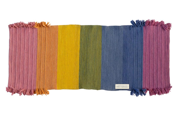 Chakra yoga mat laid flat, woven in seven bands of plant-dyed colour from rose and orange through yellow, green and blue to violet