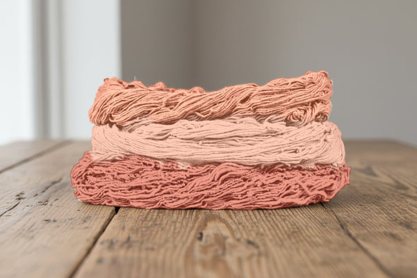 Skeins of cotton plant-dyed with Indian madder in shades of coral and peach, on a wooden table