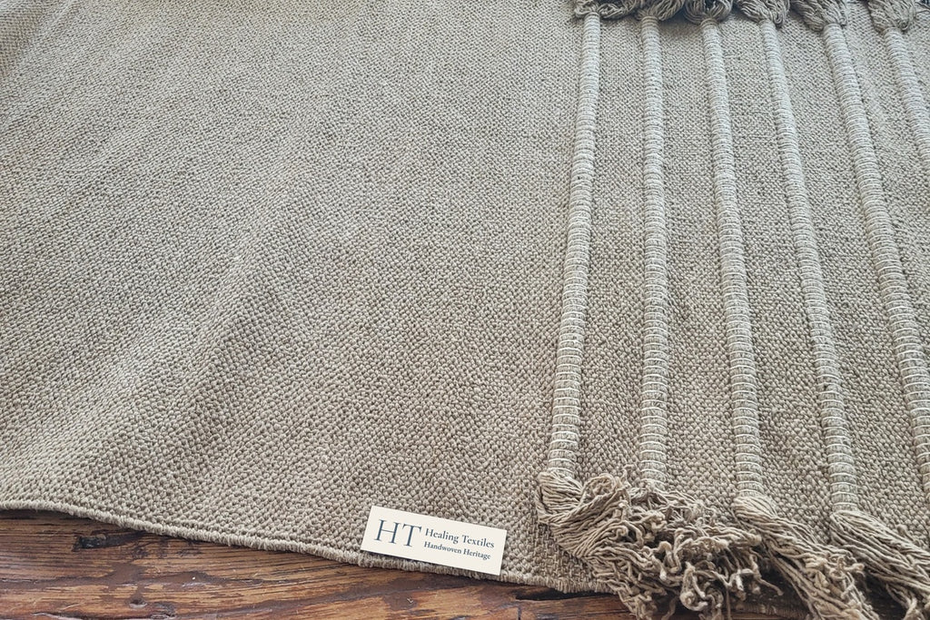 Close-up of a Myrobalan yoga mat on a wooden floor, showing the woven ridges, fringe and Healing Textiles label
