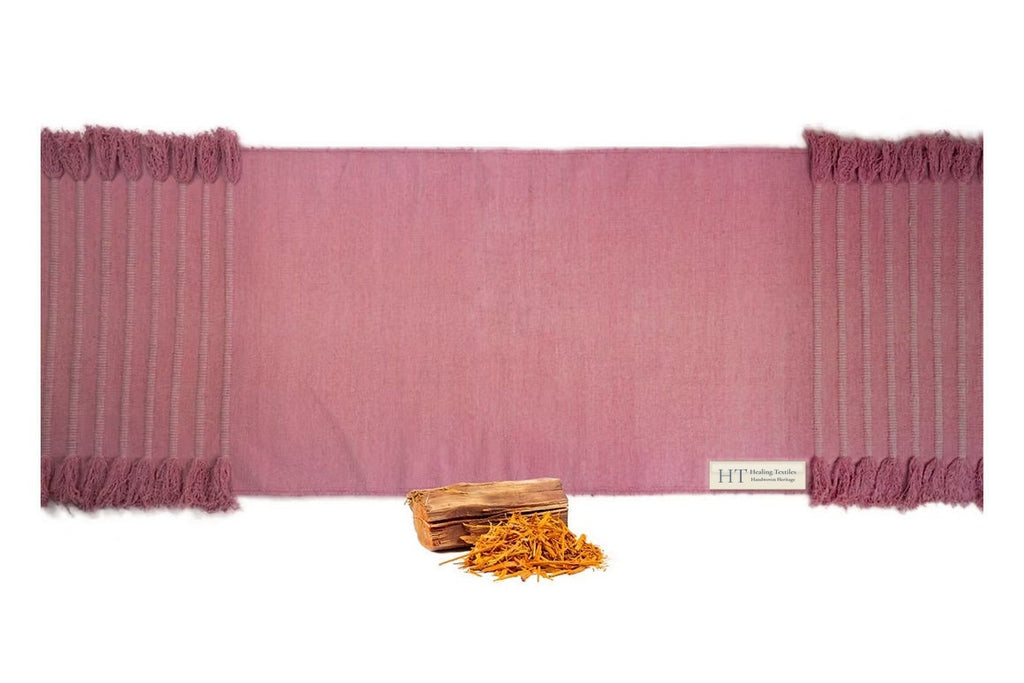 Sappanwood rose-red organic cotton yoga mat laid flat, with tasselled ends and sappanwood chips and shavings in front