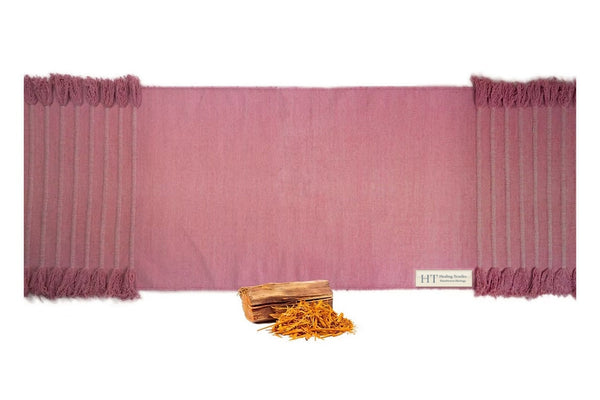 Sappanwood rose-red organic cotton yoga mat laid flat, with tasselled ends and sappanwood chips and shavings in front