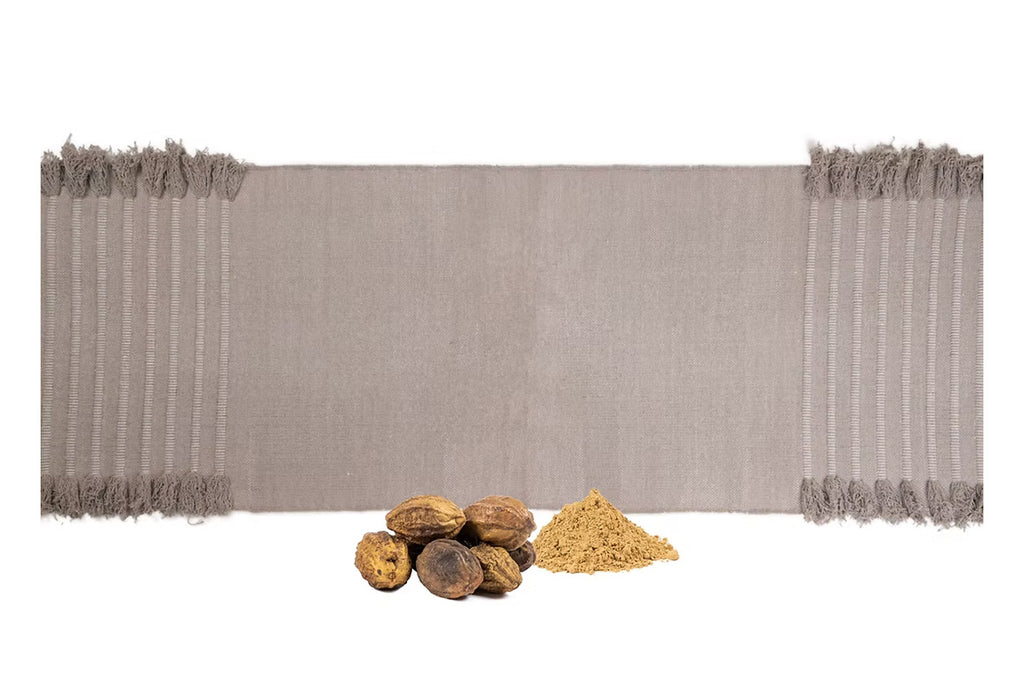 Ayurvastra yoga rug in earthy clay  displayed with powdered myrobalan and whole myrobalan nuts, showcasing the natural Ayurveda plant dyes used in the herbal textile process