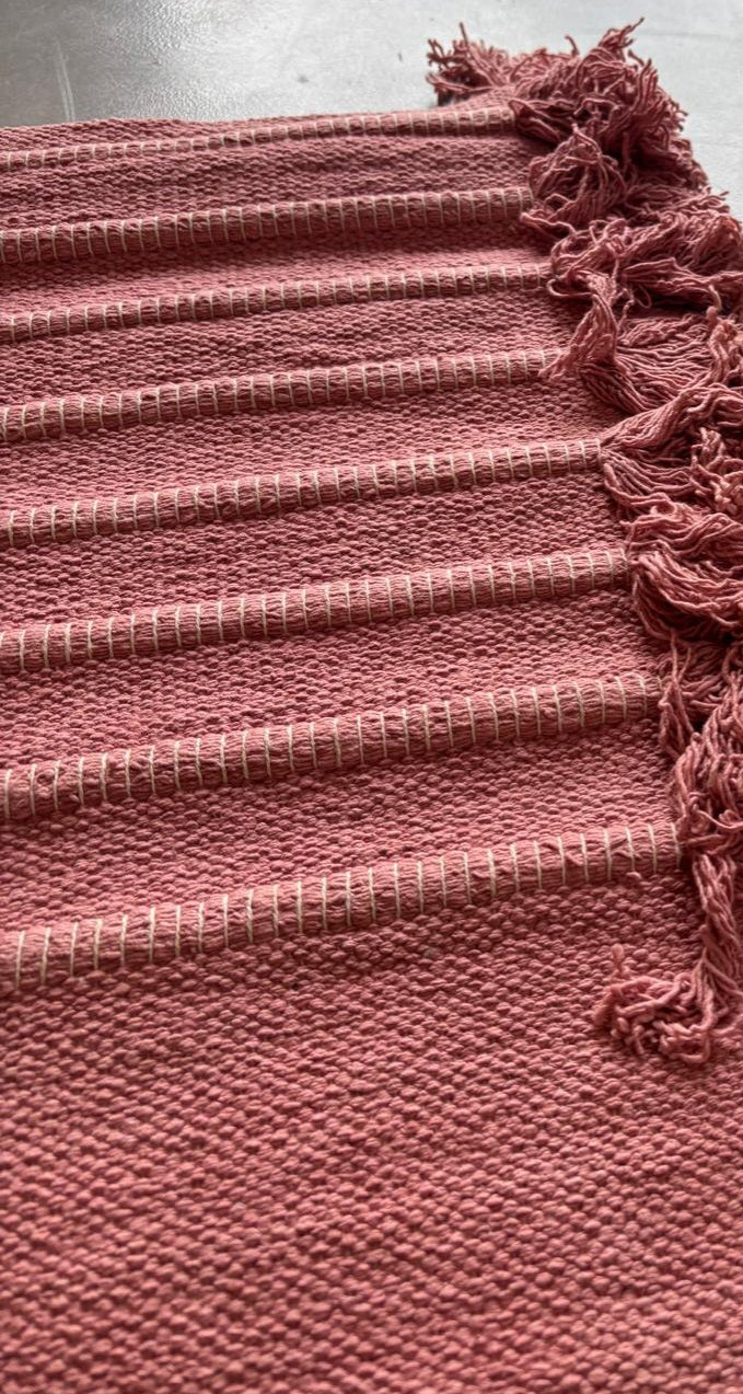 Close-up of the handloomed weave and tasselled fringe on a rose-red Sappanwood yoga mat