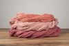 Skeins of plant-dyed cotton in coral, blush pink and deep rose, stacked on a wooden table